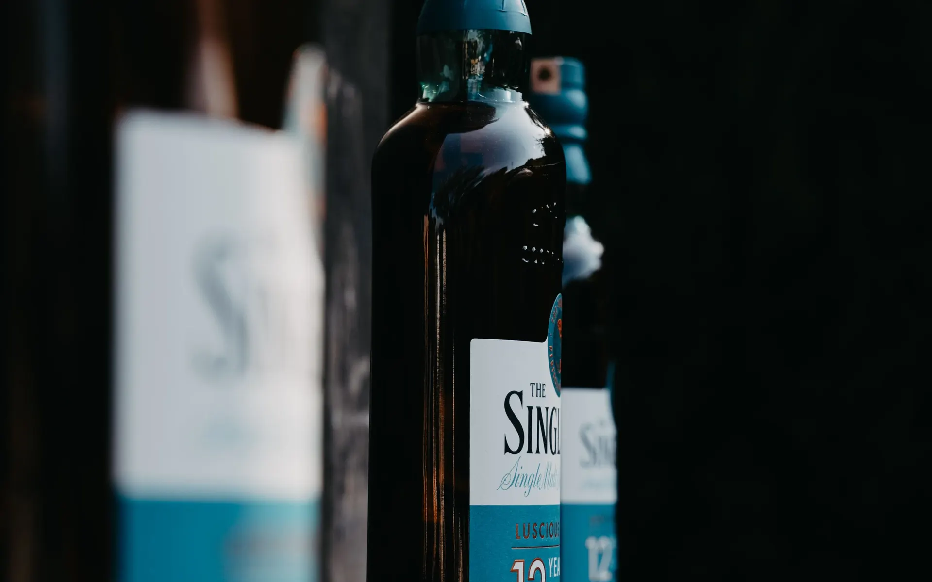 Single malt Scotch whisky bottles lined up in a moody, softly lit bar display